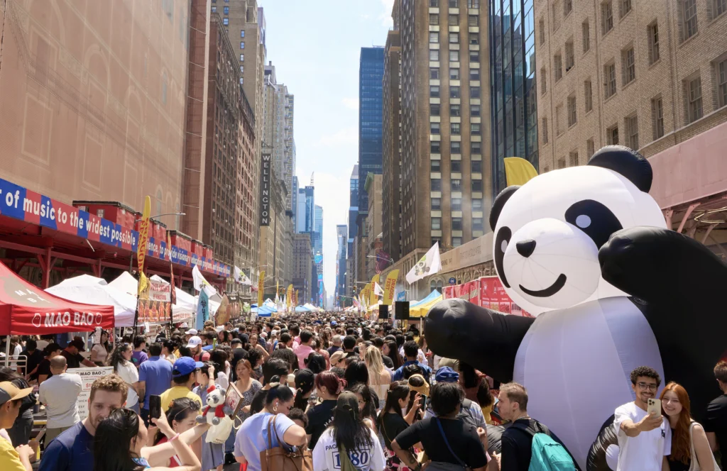 A crowded street festival with a large panda balloon.