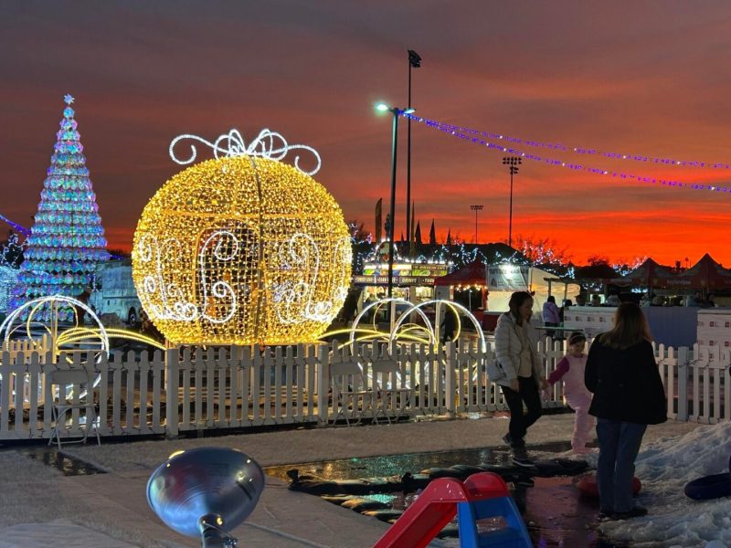 A glowing pumpkin carriage light installation at sunset with people around.