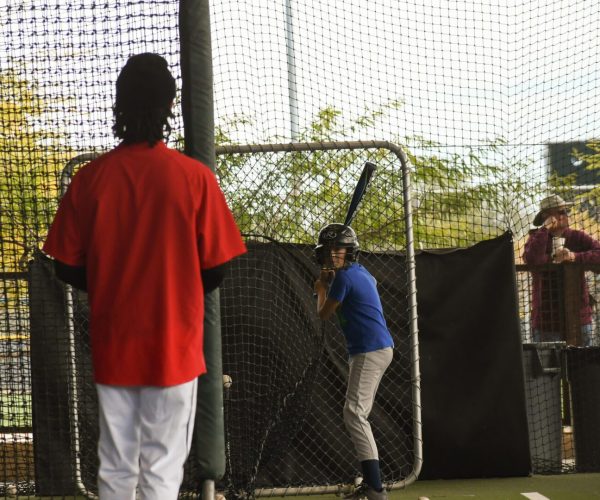 A child practices batting with adults supervising indoors.