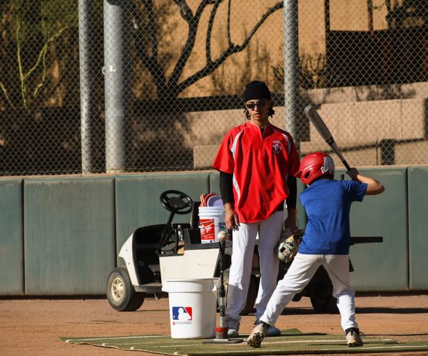 Young baseball player swings bat during practice with coach nearby.