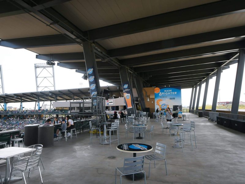 Empty outdoor seating area under a roof with scattered tables and chairs.